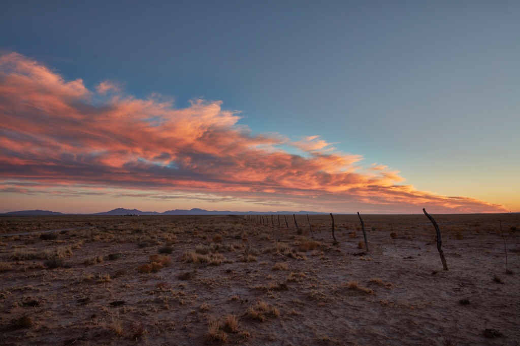 The sky reddens at sunset over the Soccoro County landscape and a line of homemade fence posts and barbed wire.